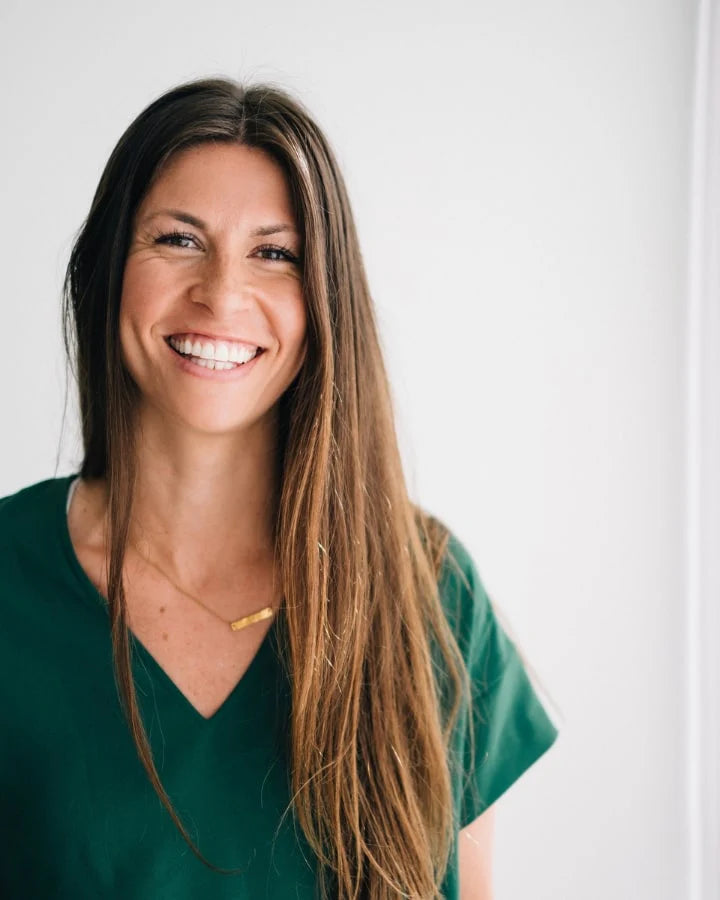 Woman with long brown hair and a green top smiling against a plain white background.